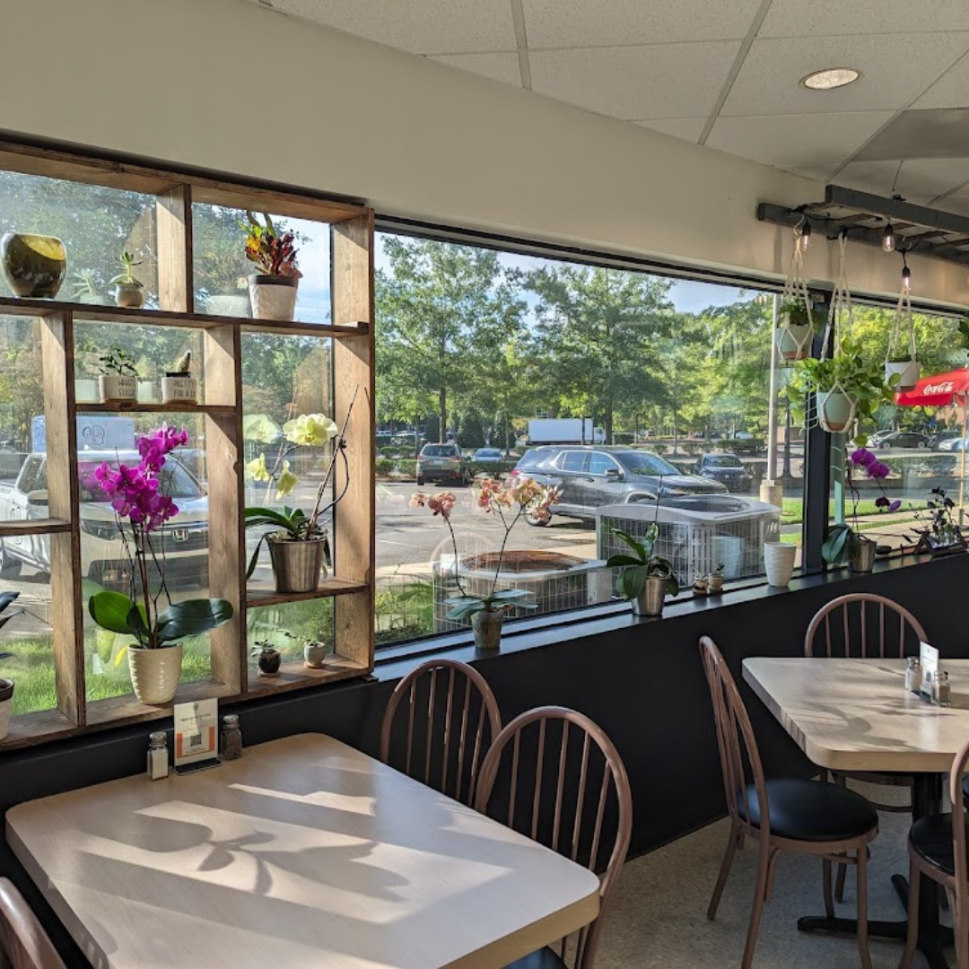 Chelsea Cafe with cozy window seating, wooden chairs, and a variety of potted plants and orchids.